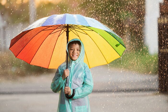 Child smiling under a colorful umbrella in rain, showcasing creative product use.