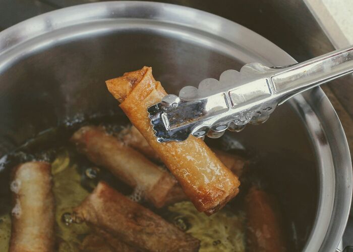 Tongs lifting fried spring rolls from oil, demonstrating products used differently than intended.