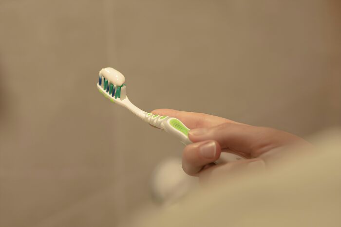 Hand holding a toothbrush with toothpaste, possibly used for a different purpose than intended.