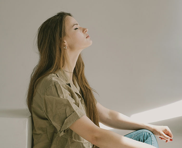 Teen deep in thought, eyes closed, sitting peacefully in sunlight.