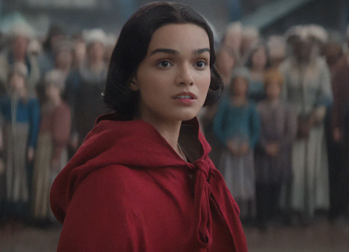 Young woman in red cloak at Disney's 'Snow White' event in Spain with crowd in background.