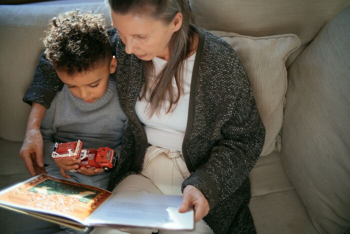 Grandmother reading a book with her grandchild on a sofa, highlighting generational bonding and family.