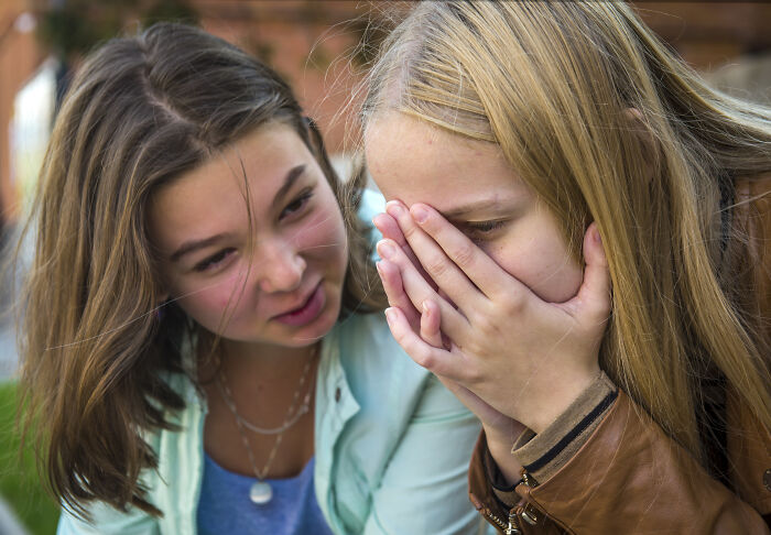 Two girls whispering, portraying telltale signs of being socially inexperienced and sheltered.