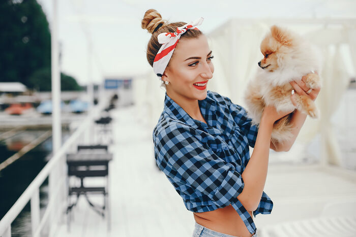 Smiling woman in plaid shirt holds a fluffy dog outdoors, illustrating signs of being raised in a cave.