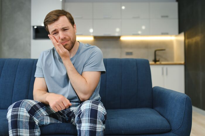 A man in pajamas looking confused while sitting on a sofa, representing signs of being raised in a cave.
