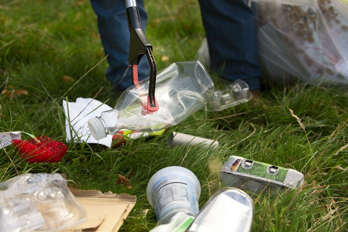 Person using a grabber tool to pick up trash in a park, highlighting telltale signs of littering.