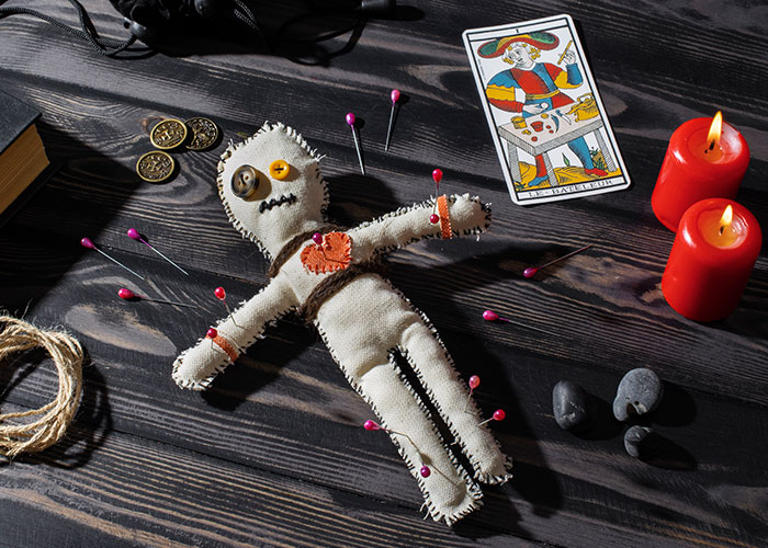 Voodoo doll with pins, tarot card, and candles on a dark table, reflecting uncaring friendship.