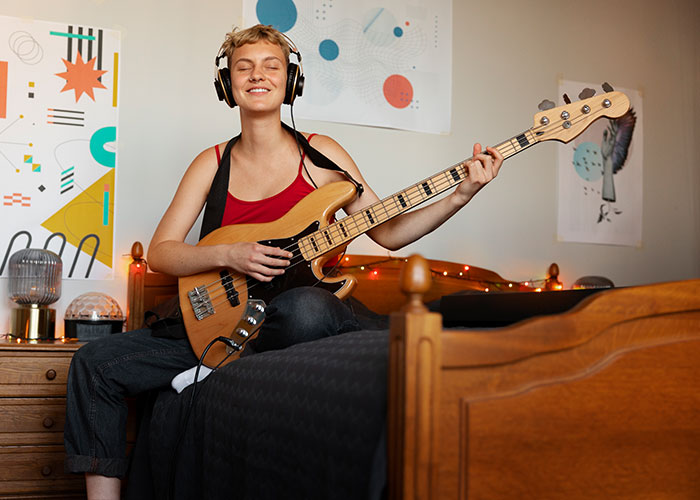 Person in headphones playing bass guitar, relaxed in a room.