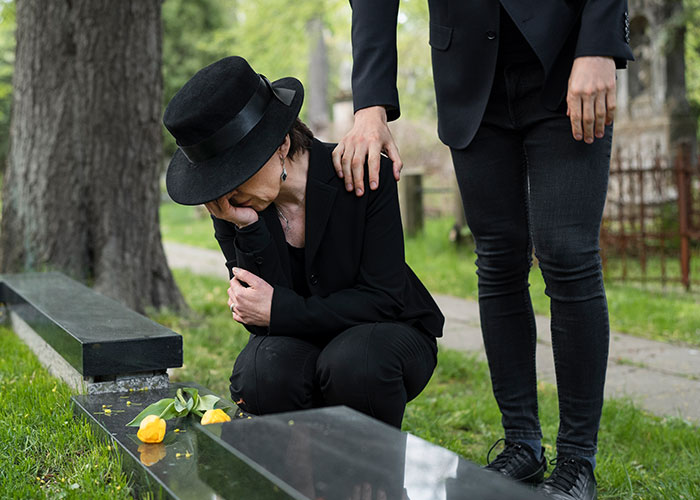 A grieving woman in black at a gravesite, with a comforting hand from a friend who doesn't care about her.