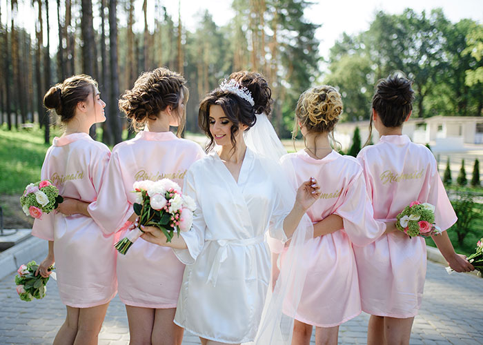 Bride with bridesmaids in pink robes holding bouquets, highlighting themes of friendship and care.