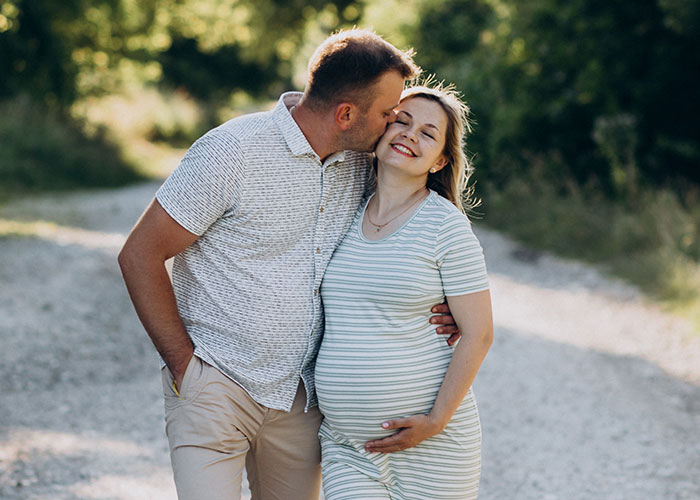 Pregnant woman joyful with partner on a sunny path, expressing genuine friendship and care.