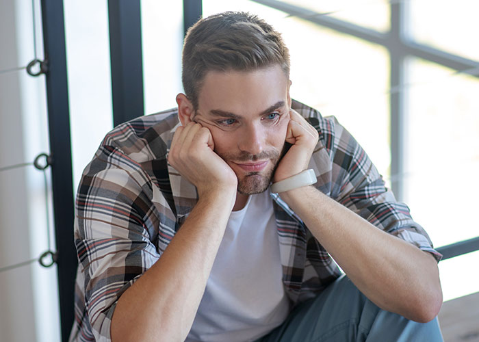 Man in plaid shirt sitting pensively, reflecting on uncaring friend.