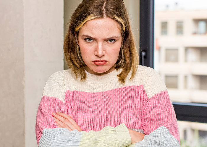 Person with arms crossed, looking upset, reflecting on a friend's lack of care against an urban backdrop.