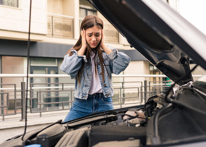 Woman frustrated with car breakdown, feeling abandoned and uncared for.