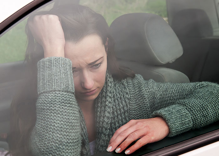 Woman in a car, reflecting on a friend's lack of care, wearing a green sweater and looking pensive.