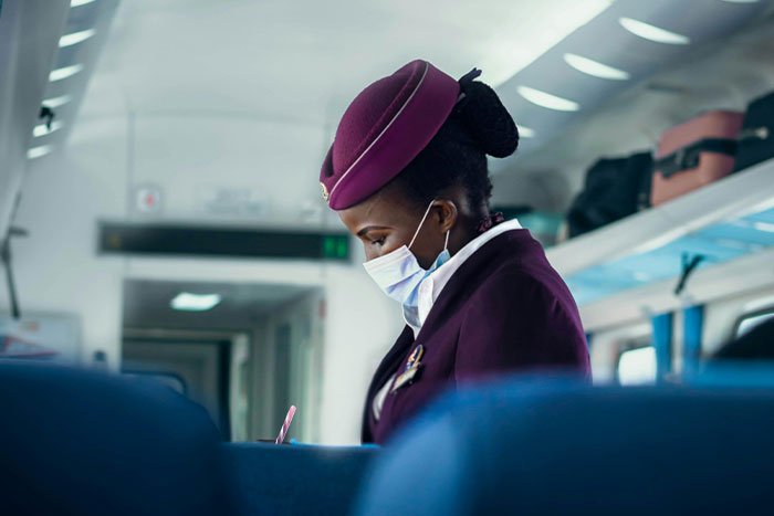 Airline attendant in uniform and mask onboard, checking documents mid-flight.