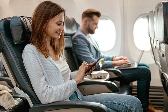 Airplane passengers seated, one using a phone, the other a laptop, highlighting seat choice options and comfort.