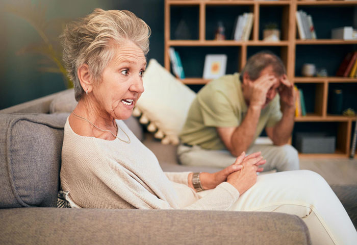 Elderly woman looking upset on sofa, discussing family history tradition.