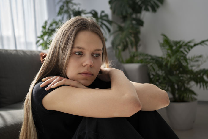 Young woman sitting indoors, appearing thoughtful, with a focus on social anxiety.