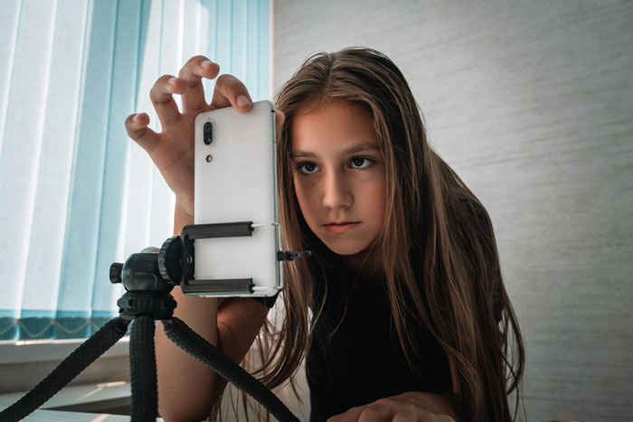 Young person setting up a smartphone on a tripod, focusing on recording content.