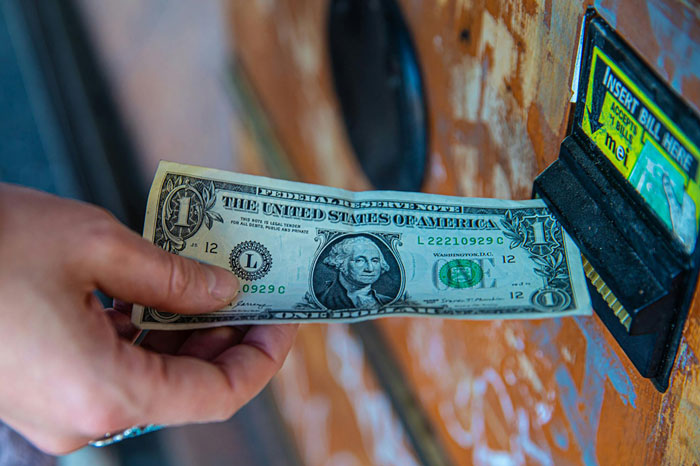 Hand inserting a dollar bill into a machine, illustrating exchanging money and financial transactions.
