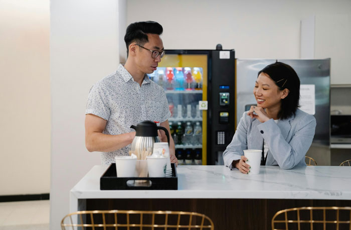 Two colleagues chatting casually over coffee in an office break room.