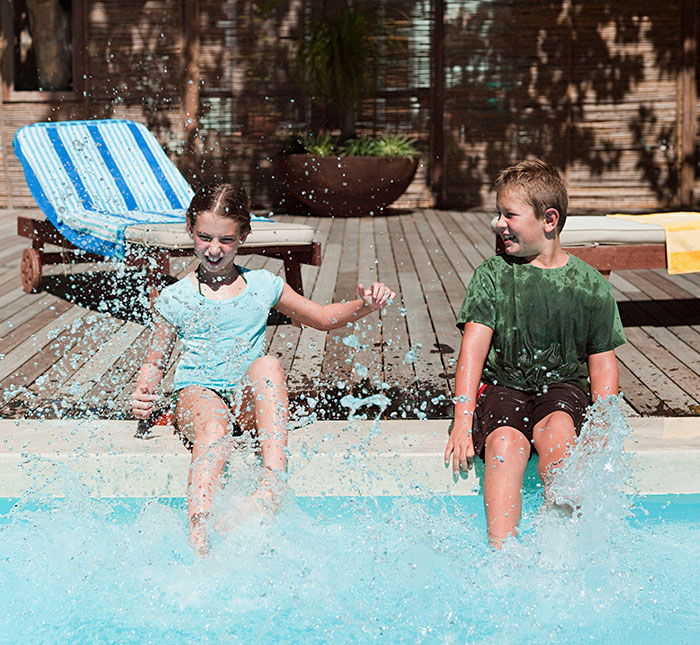 Kids splashing water at a pool, enjoying a sunny day while sitting at the edge.