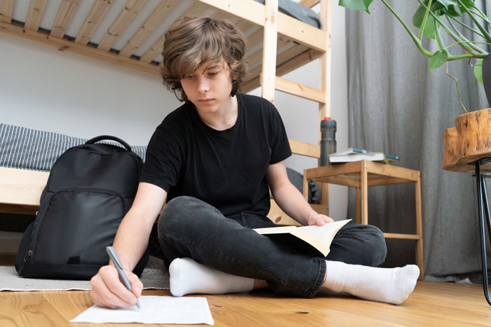 Teen boy studying on the floor in casual attire, highlighting family tension over college fund decisions.