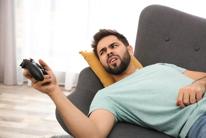 Man on a couch holding a game controller, looking frustrated, focused on video games instead of parenting responsibilities.