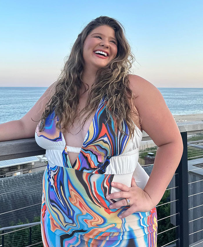Plus-size influencer in a colorful dress smiling by the ocean.