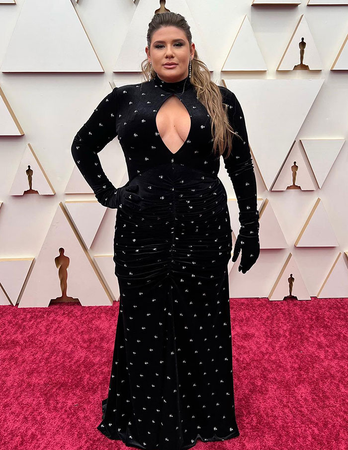 Plus-size influencer in a black gown at a red carpet event, standing confidently.