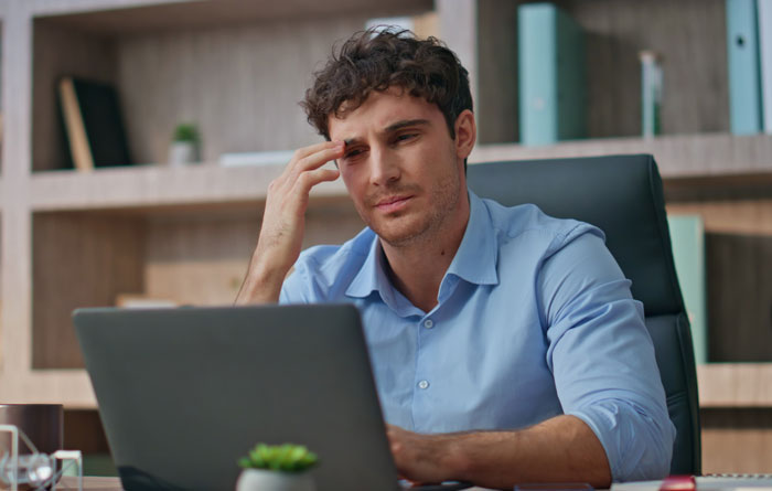 Man concerned at laptop, contemplating reporting coworker cheating in a walking competition, in a home office setting. Man concerned at laptop, contemplating reporting coworker cheating in a walking competition, in a home office setting.