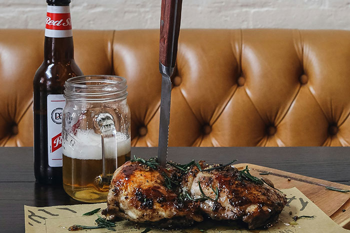 Grilled chicken with herbs and a knife, next to a beer bottle, evoking memories from restaurants that don't exist today.