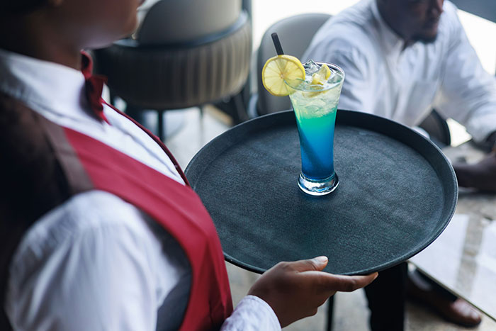 Waiter serving blue cocktail with lemon in a nostalgic restaurant setting.