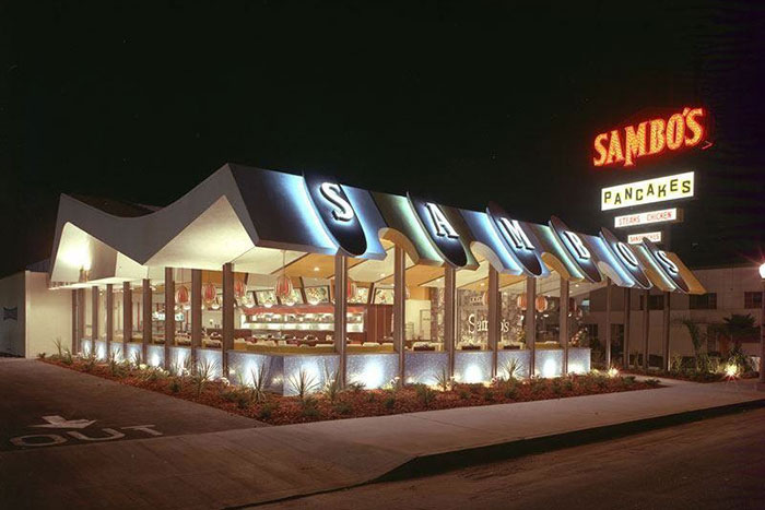 Exterior of Sambos, a restaurant that doesn't exist today, with retro signage and large windows glowing at night.