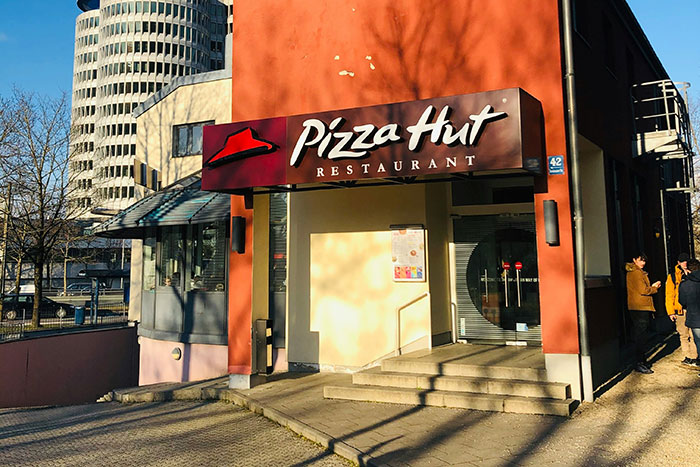 Pizza Hut restaurant exterior with signage, sunlight casting shadows on the building.