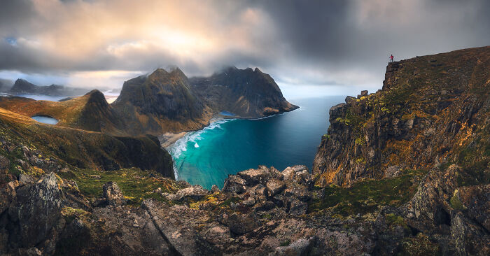 Photographer captures stunning landscapes with a dramatic coastal view and cloudy skies, featuring a lone hiker on a cliff.