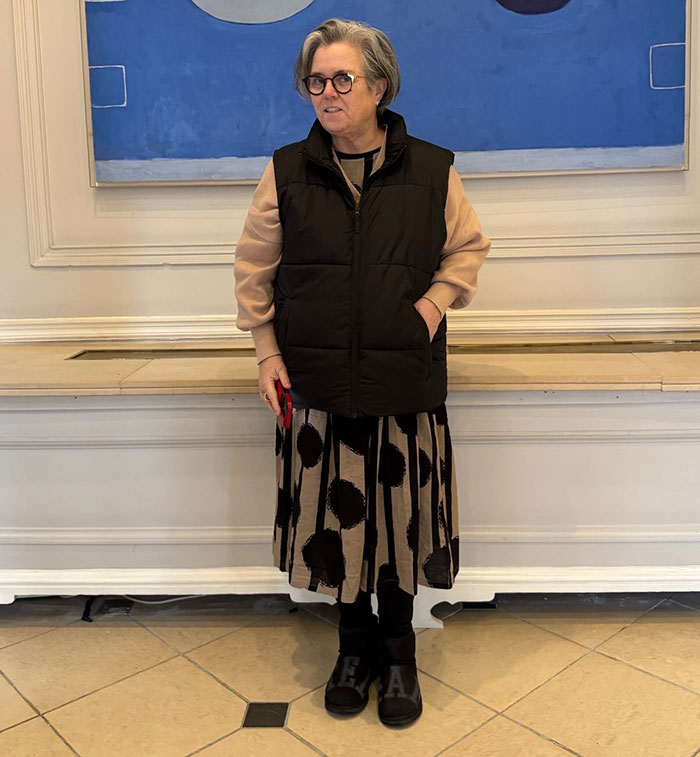 Person in a stylish outfit stands indoors in front of a blue abstract painting, related to move to Ireland.