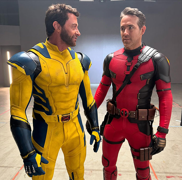 Hugh Jackman in a yellow superhero costume, potentially linked to Blake Lively drama, standing with a man in a red suit.