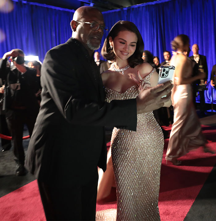 Behind the scenes at Oscars 2025, two attendees take a selfie on the red carpet.