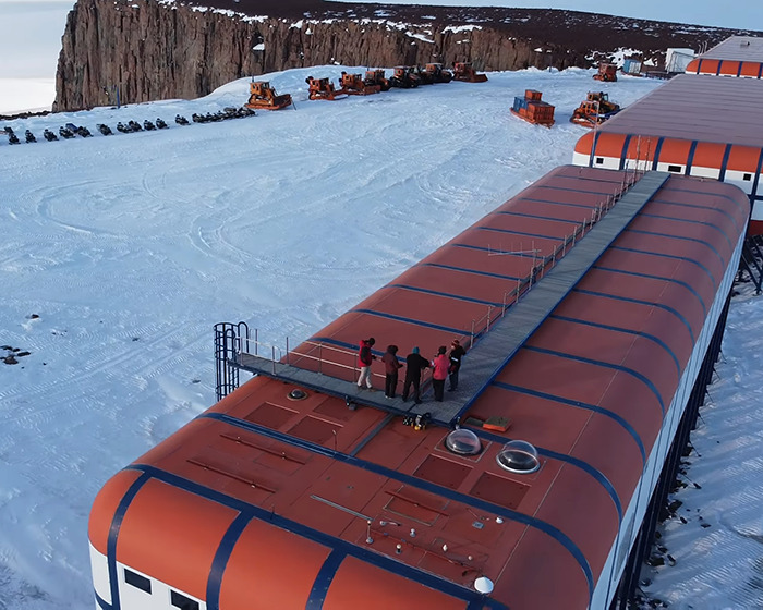 Remote Antarctica base with people on the roof, surrounded by snow and machinery, highlighting a desolate setting.