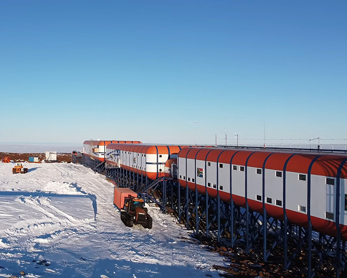 Remote Antarctica base facility with connected modular units on a snowy landscape under a clear blue sky.
