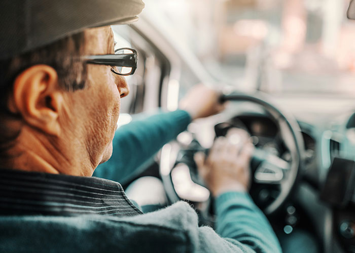 Man in glasses driving a car, possibly having a "need to leave right now" experience, focused on the road ahead.
