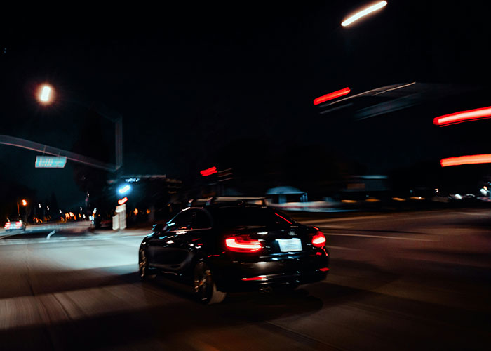 A car speeding through a dark city street at night, blurred lights emphasizing a sense of urgency and escape.
