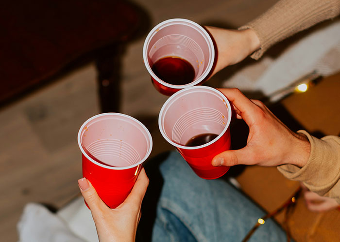 Three people toasting with red cups at a party, capturing a moment before an unsettling experience.