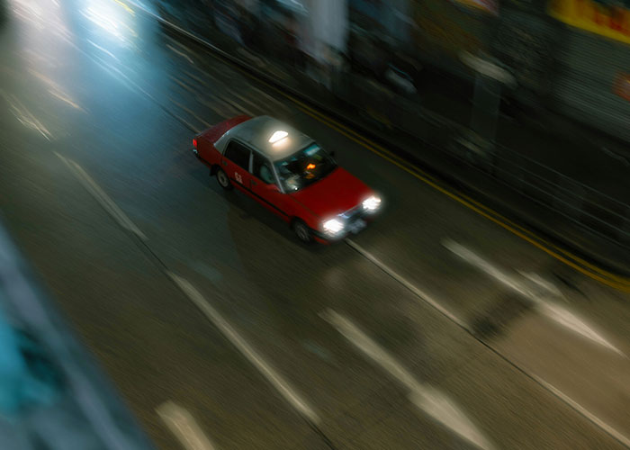 Red taxi speeding down a dimly lit city street at night, evoking a sense of urgency to leave quickly.