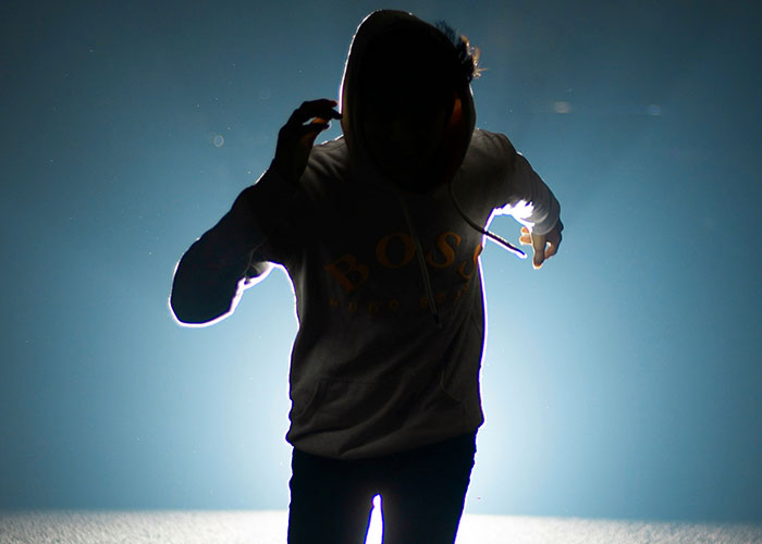 A silhouetted person in a hoodie running towards the camera in a dramatic, dimly lit setting.