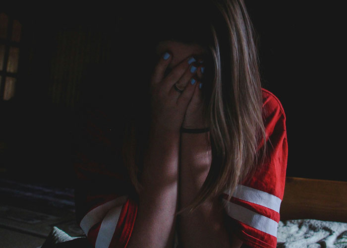 Person in a dimly lit room covering face, depicting a scary need-to-leave moment experience.