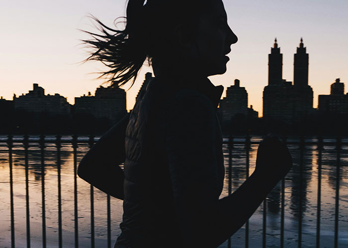Silhouette of a woman running along a city waterfront at dusk, conveying an urgent need to leave.