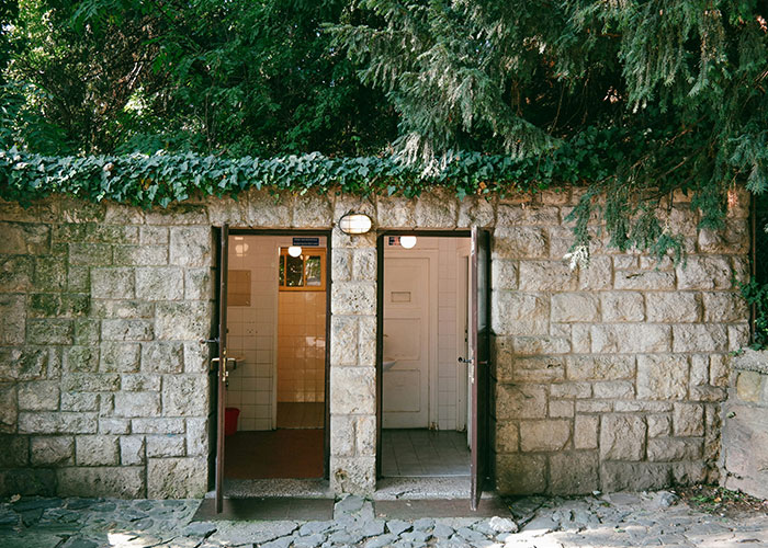 Old stone building with two open doors, revealing a dimly lit interior, evoking a sense of urgency to leave quickly.